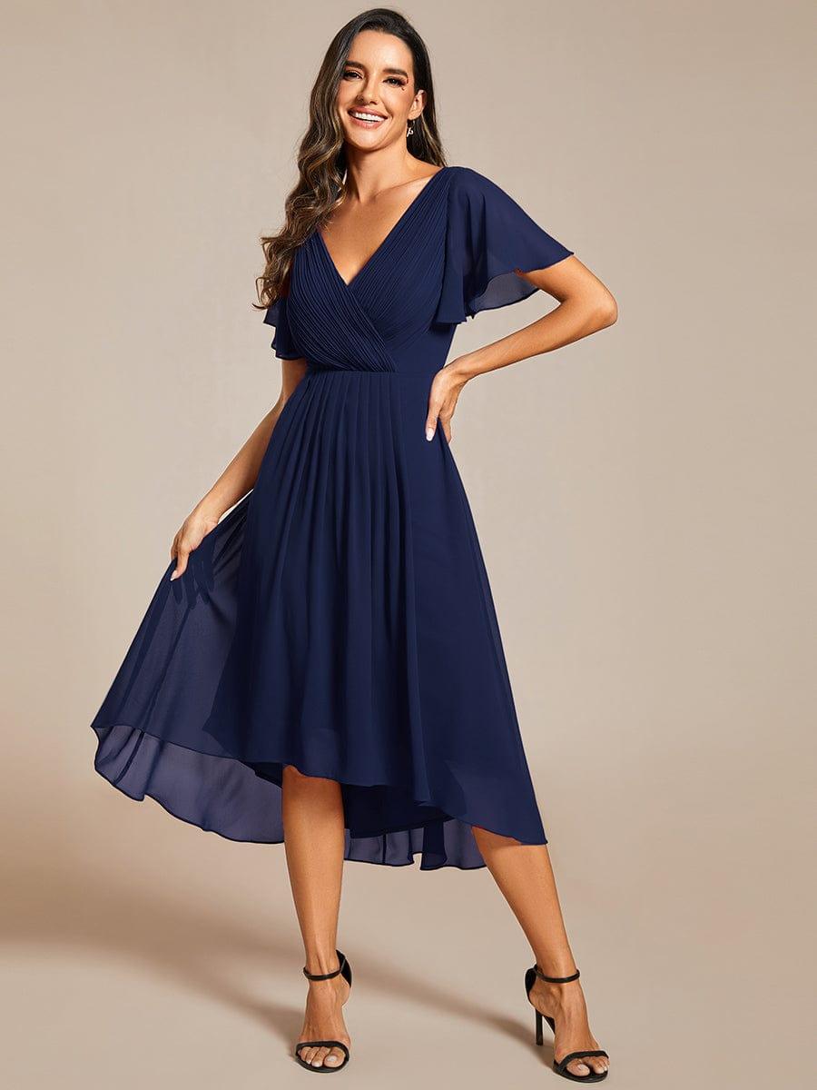 Model im marineblauen Chiffonkleid hält den Rock mit einer Hand an, Vorderansicht mit Hoch-Tief-Saum und schwarzen Sandalen. 54