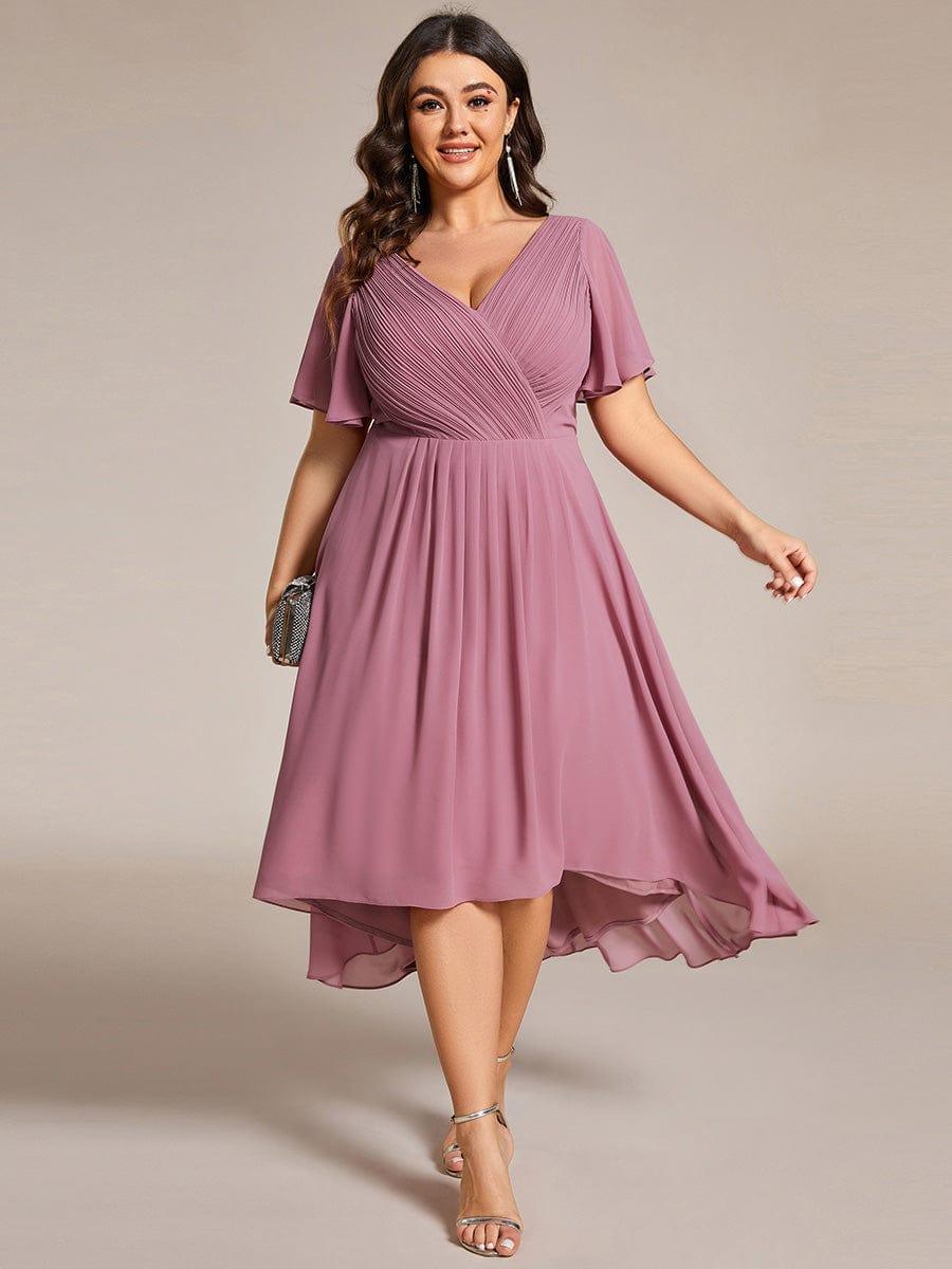 Curvy-Model trägt das mauvefarbene Kleid mit gerafftem V-Ausschnitt und asymmetrischem Saum, in der Hand eine kleine glitzernde Clutch. 63