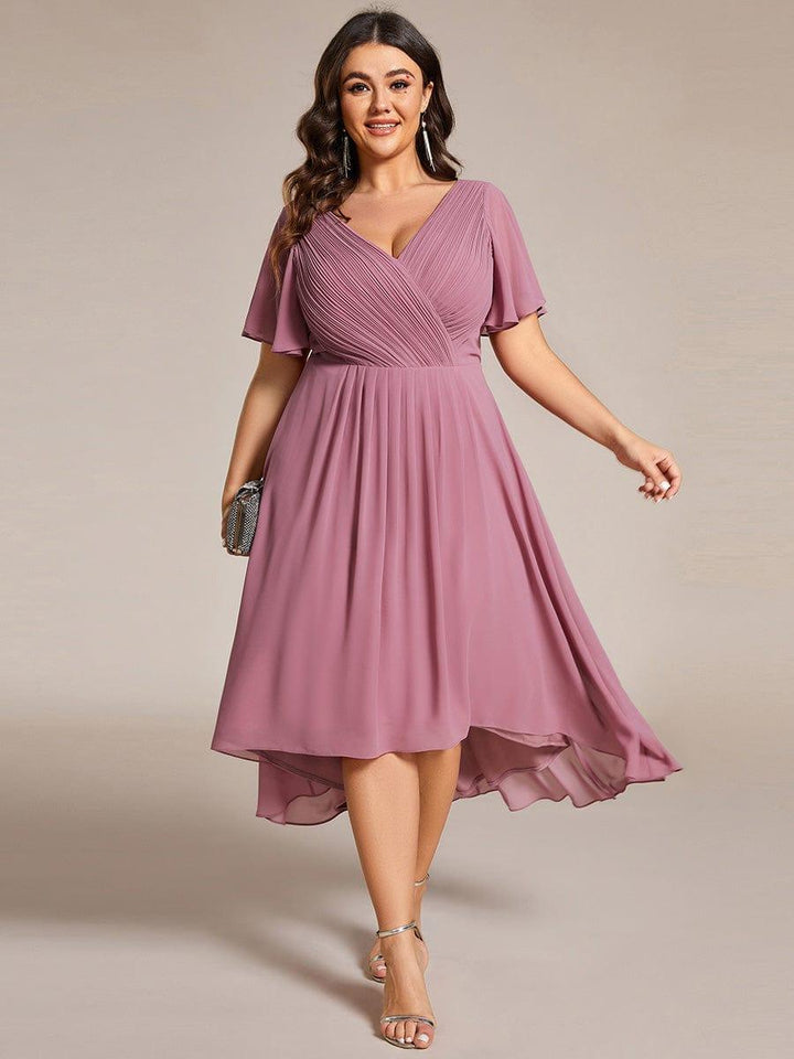 Curvy-Model trägt das mauvefarbene Kleid mit gerafftem V-Ausschnitt und asymmetrischem Saum, in der Hand eine kleine glitzernde Clutch. 63