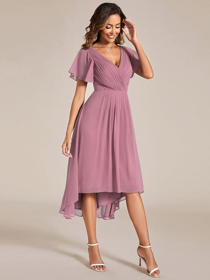 Mauvefarbenes Chiffonkleid in Ganzkörperansicht am Model, mit Wickeloberteil, Flatterärmeln und vorne kürzerem, hinten längerem Saum, dazu helle Sandaletten. 62