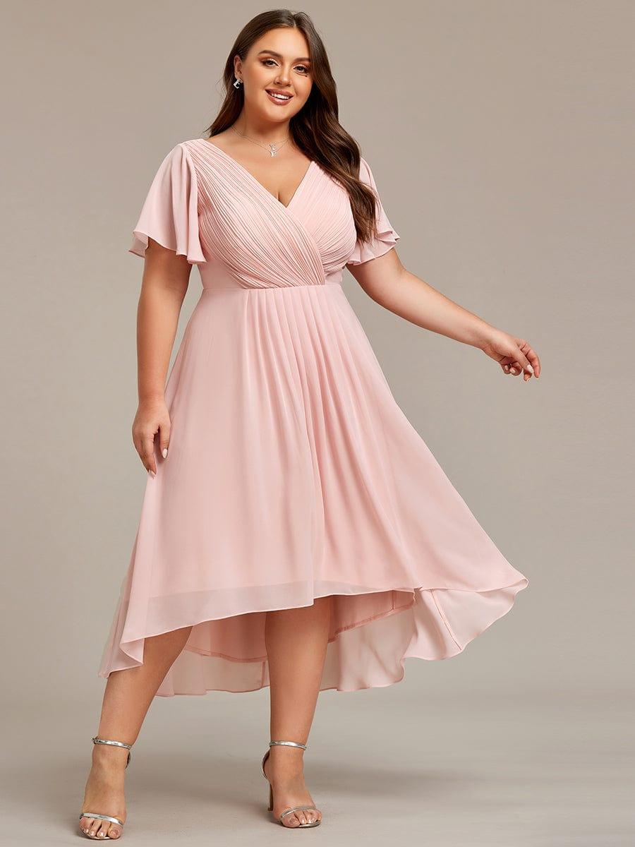 Curvy Model im rosafarbenen Kleid, lächelnd in leichter Drehung, ein Arm zur Seite gestreckt, der Chiffonsaum weht asymmetrisch. 34