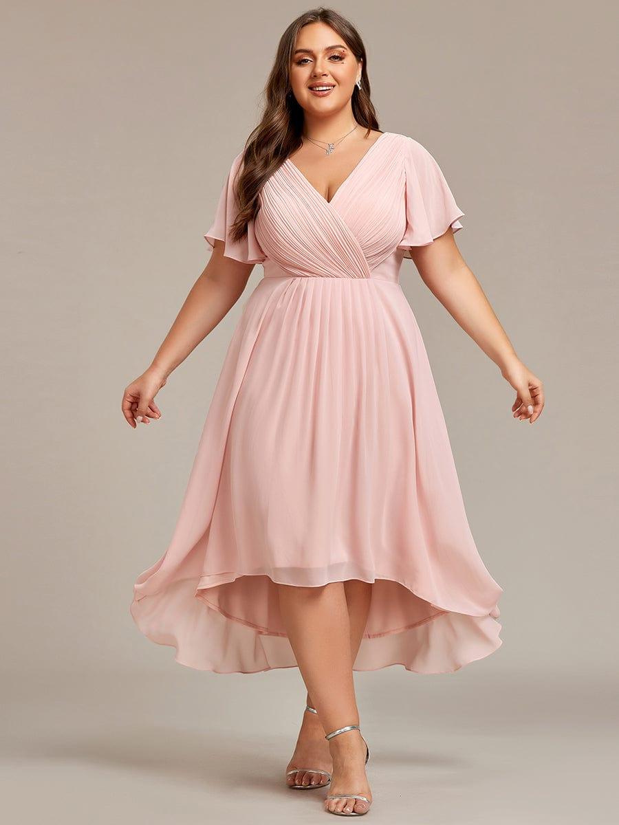 Curvy Model im rosafarbenen Chiffonkleid frontal mit leicht ausgebreiteten Armen, zu sehen sind das Wickeloberteil und der wellige Hoch-Tief-Saum. 35