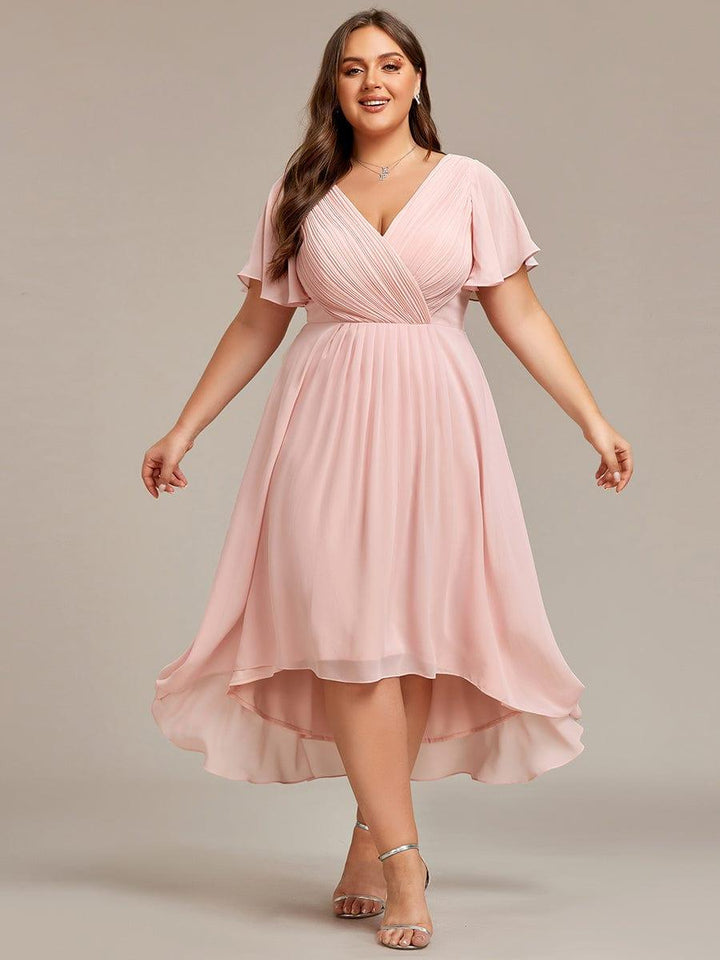 Curvy Model im rosafarbenen Chiffonkleid frontal mit leicht ausgebreiteten Armen, zu sehen sind das Wickeloberteil und der wellige Hoch-Tief-Saum. 35