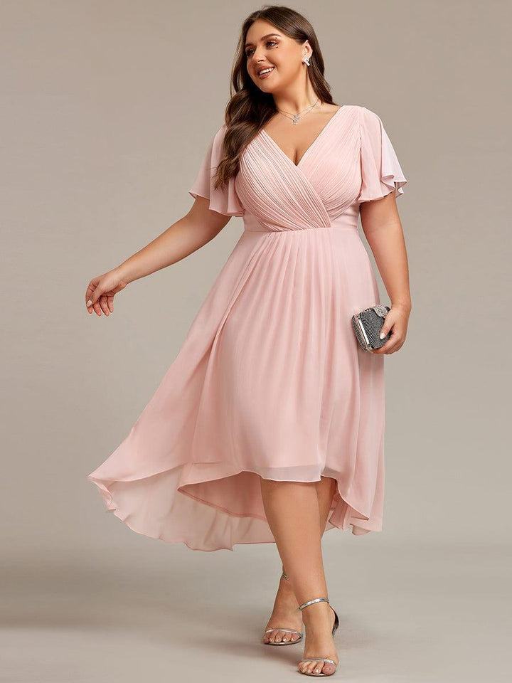 Curvy Model im rosafarbenen Chiffonkleid mit V-Ausschnitt und Flatterärmeln, dazu silberne Sandaletten und Glitzerclutch, der Rock schwingt seitlich. 31