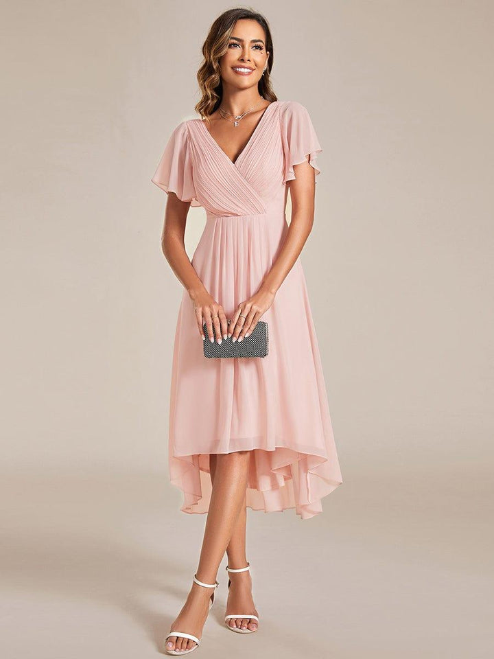 Frontansicht in Rosa mit gerafftem V-Oberteil und Flatterärmeln, Model hält eine dunkle Clutch mit beiden Händen vor sich. 15