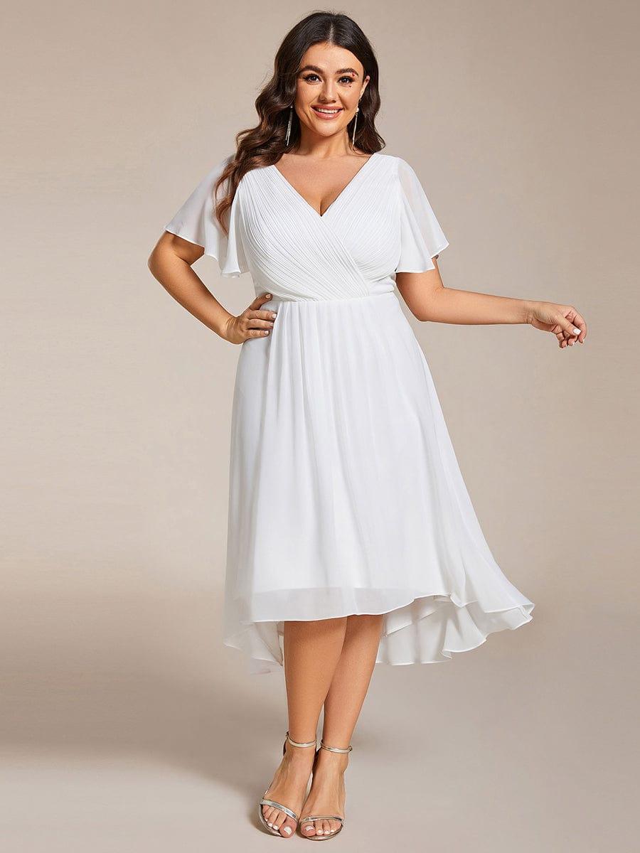 Curvy-Model trägt das weiße Chiffonkleid mit Wickeloberteil, Flatterärmeln und Hoch-Tief-Saum, die Hand an der Hüfte, dazu silberne Sandaletten. 73
