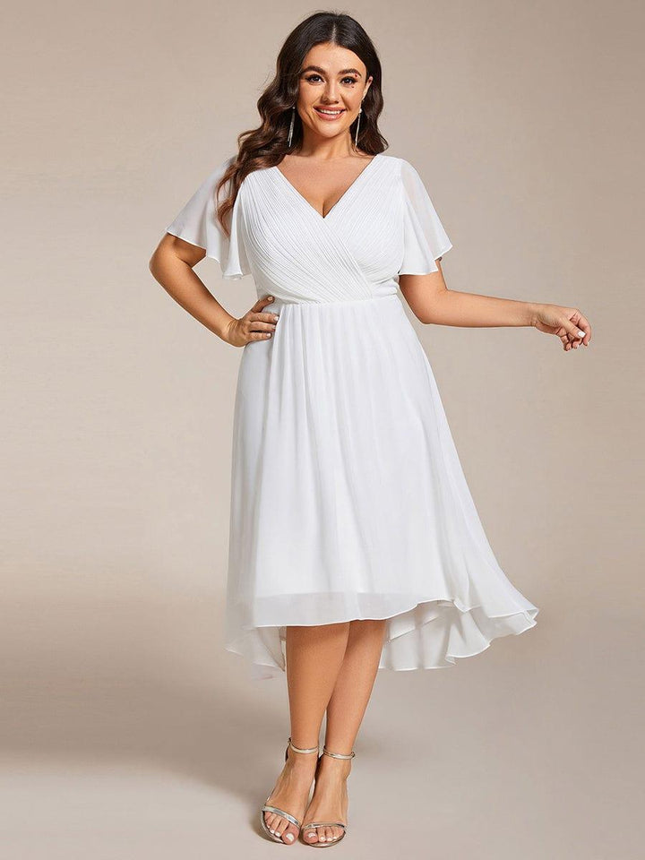 Curvy-Model trägt das weiße Chiffonkleid mit Wickeloberteil, Flatterärmeln und Hoch-Tief-Saum, die Hand an der Hüfte, dazu silberne Sandaletten. 73