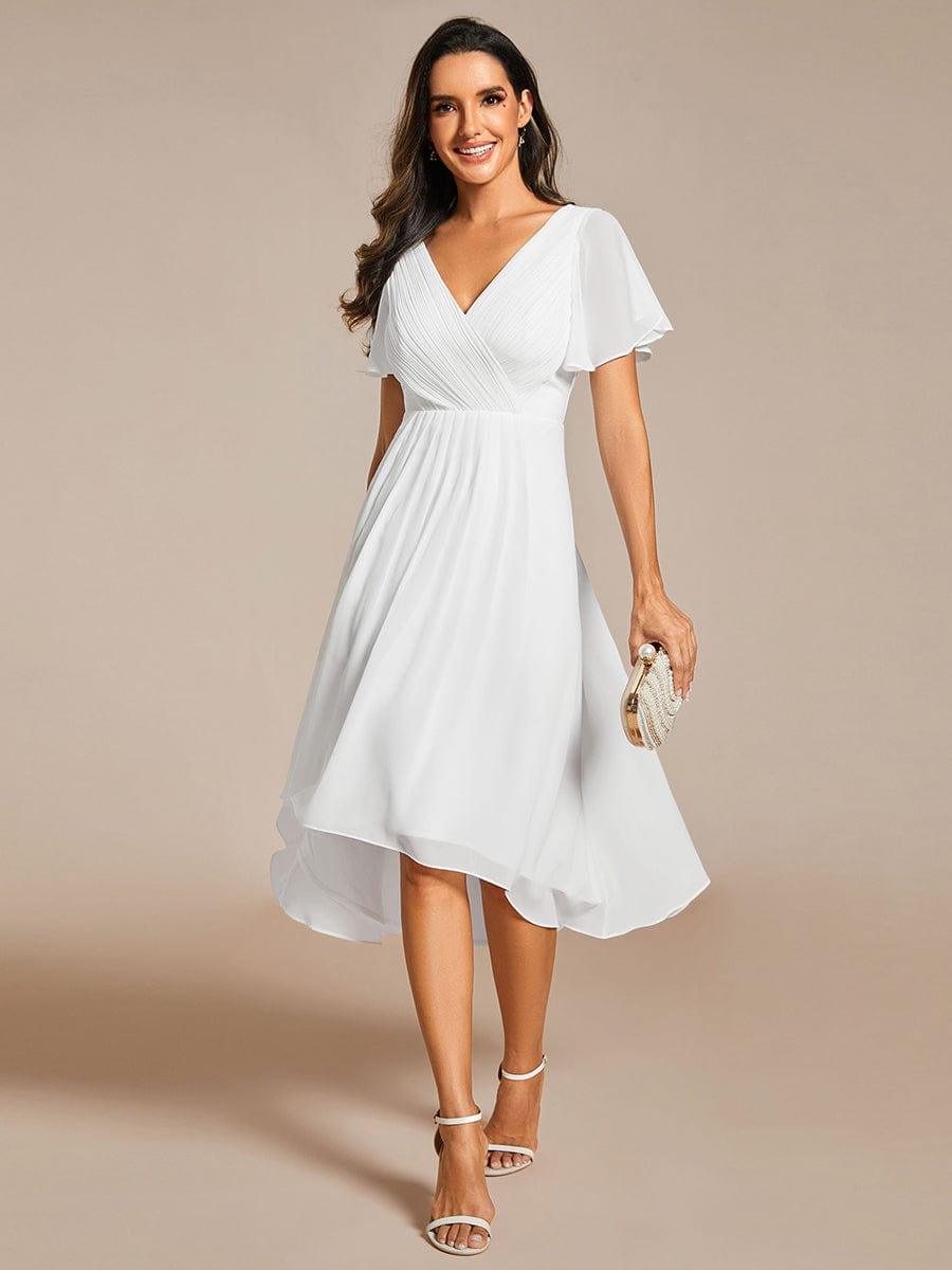 Weißes Chiffonkleid in Ganzkörperansicht am Model, mit V-Ausschnitt, Flatterärmeln und asymmetrischem Saum, dazu eine perlenbesetzte Clutch und helle Sandalette 68
