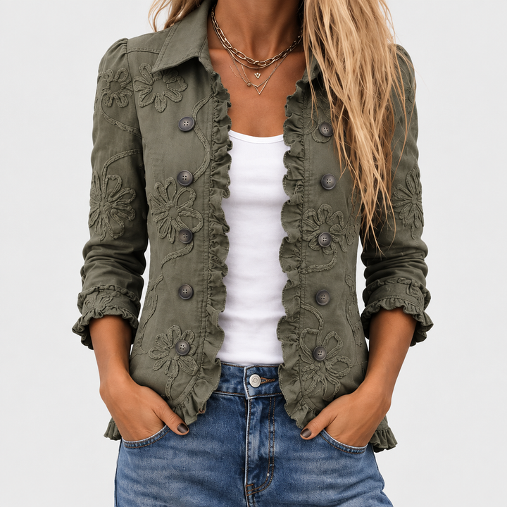 Nahaufnahme der offenen olivgrünen Jacke an einem Model, mit Blütenstickerei, Rüschenkante, Knöpfen, weißem Top und Jeans. 1