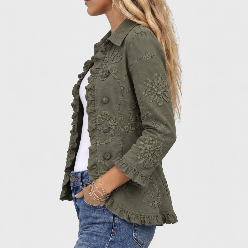 Seitenansicht der Jacke am Model, mit Blumenstickerei am Ärmel, Rüschen am Saum und an der Manschette, Hand in der Hosentasche. 4
