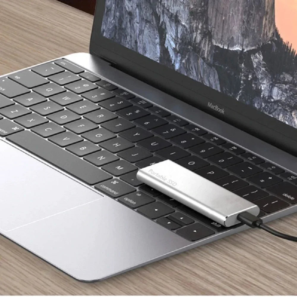 Silberne Festplatte liegt per Kabel angeschlossen auf der Tastatur eines silbernen Laptops auf einem Holztisch. 7