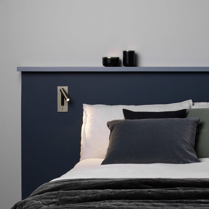 Leuchtende Wandleuchte über dem Kopfteil eines Bettes mit dunkelblauer Wand und grauen Kissen 30