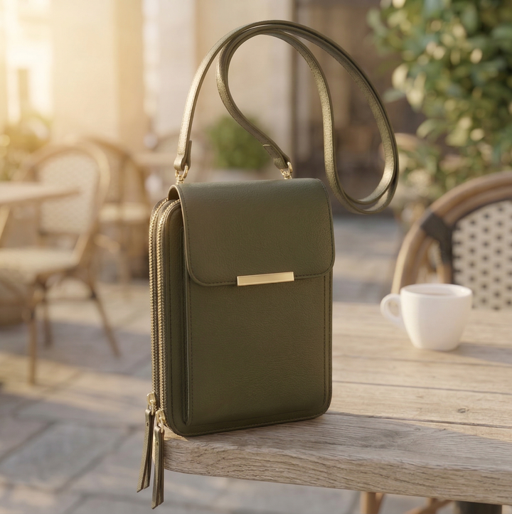 Die Tasche in dunklem Olivgrün mit goldener Spange und zwei Reißverschlussquasten, auf einem Holztisch im Freien. 5