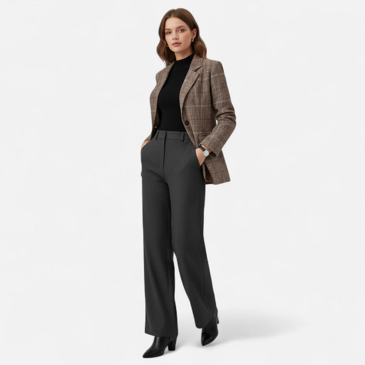Model in ganzer Figur trägt den karierten Blazer offen zu schwarzem Oberteil, grauer Stoffhose und schwarzen Stiefeletten, Hände in den Taschen. 2
