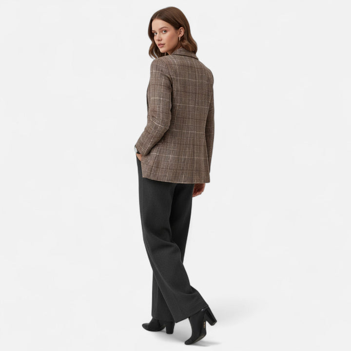 Rückansicht des Blazers an einem Model in ganzer Figur, das über die Schulter blickt, dazu graue Hose und schwarze Stiefeletten. 3