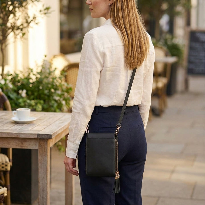 Rückansicht einer Frau mit der schwarzen Crossbody-Tasche an der Hüfte; die glatte Rückseite und der Riemen sind zu sehen. 8