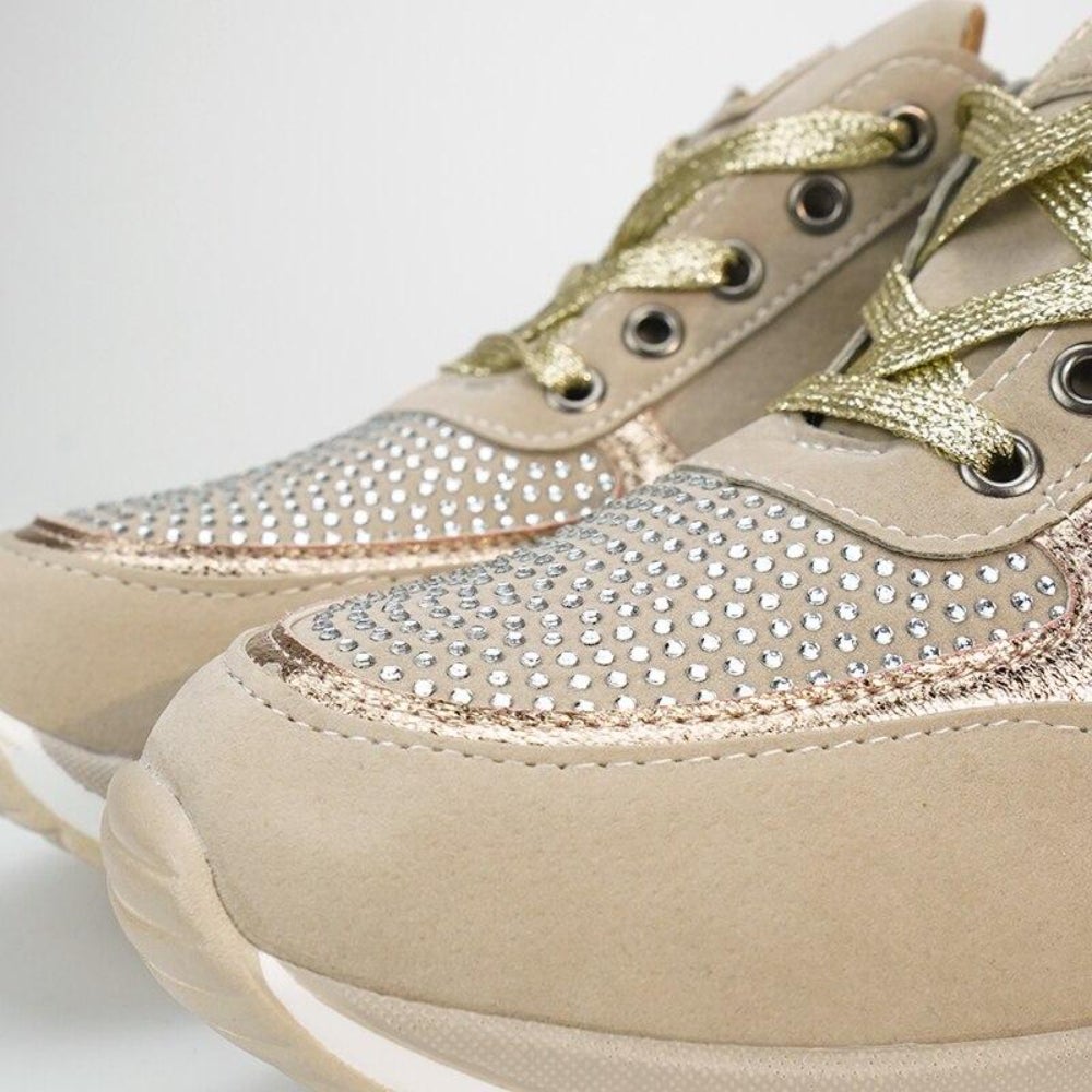 Nahaufnahme der Schuhspitzen mit dichtem Strassbesatz, goldfarbenen Schnürsenkeln, Metallösen und glänzenden Einsätzen am beigen Schuh. 10