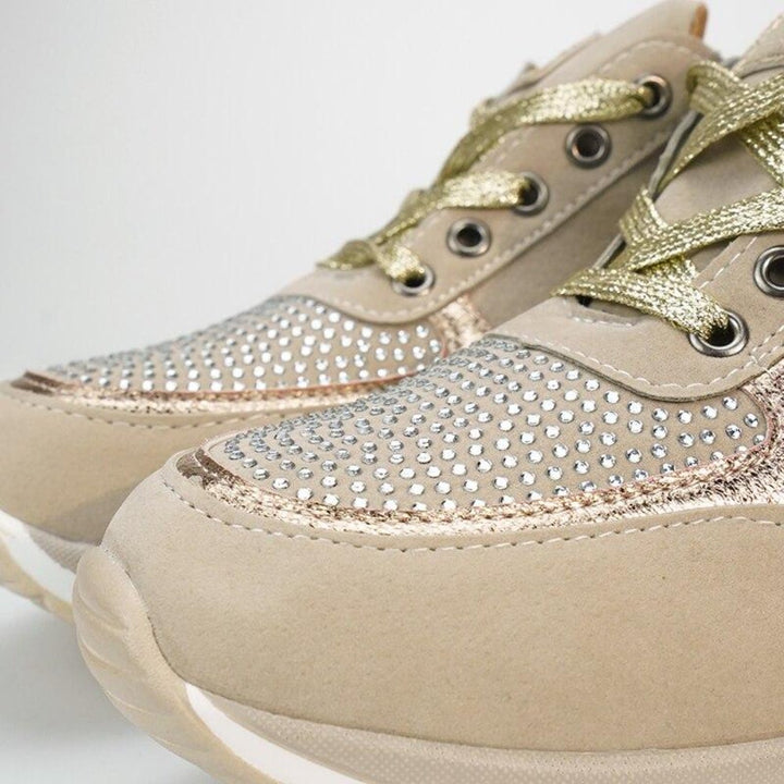 Nahaufnahme der Schuhspitzen mit dichtem Strassbesatz, goldfarbenen Schnürsenkeln, Metallösen und glänzenden Einsätzen am beigen Schuh. 10