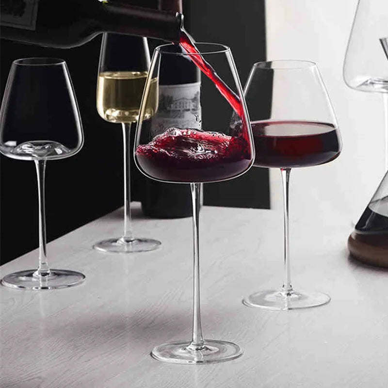Rotwein wird in ein Glas gegossen, daneben Gläser mit Weißwein und Rotwein auf einem Tisch 2