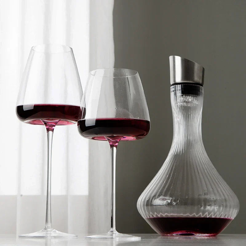 Zwei Gläser mit Rotwein neben einer gerillten Karaffe mit Metallaufsatz vor einem hellen Vorhang 3