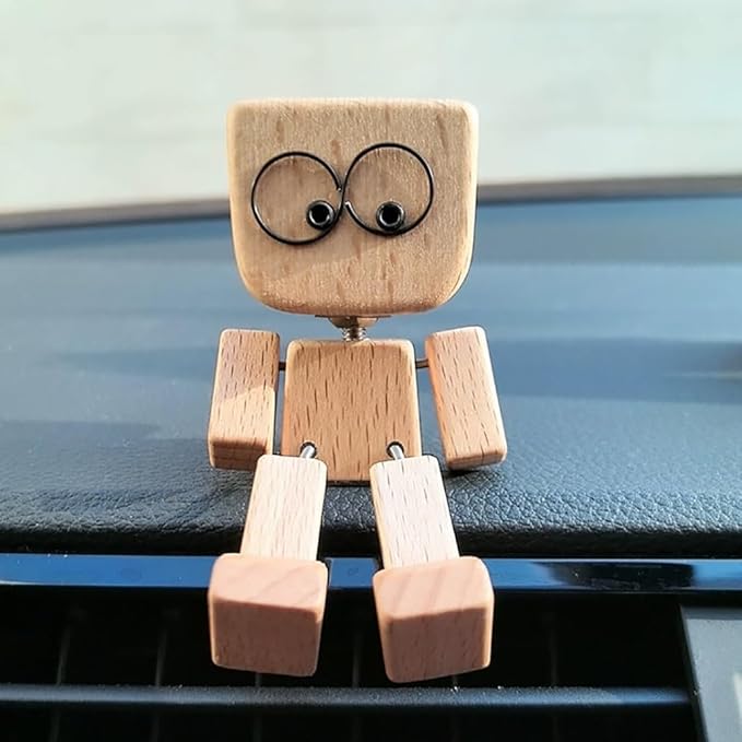 Frontansicht der Holzfigur mit großen Augen, die mit herabhängenden Beinen am Rand des Armaturenbretts sitzt, Lüftungsschlitze darunter. 4