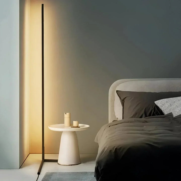 Schlanke schwarze Stehlampe leuchtet warm neben einem weißen Beistelltisch und einem Bett mit dunkler Bettwäsche 1