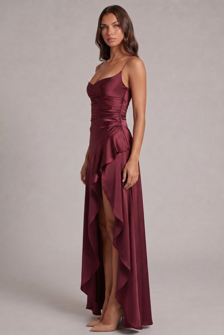 Weinrotes Maxikleid in Seitenansicht mit seitlicher Raffung, hohem Beinschlitz und fließendem Volant, getragen mit nudefarbenen Pumps. 3