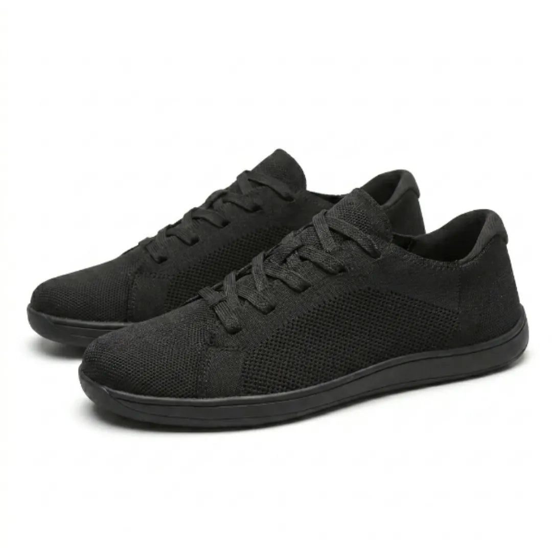 Paar schwarzer Mesh-Sneaker schräg von der Seite, nebeneinander stehend, mit Schnürung und flacher schwarzer Sohle. 16
