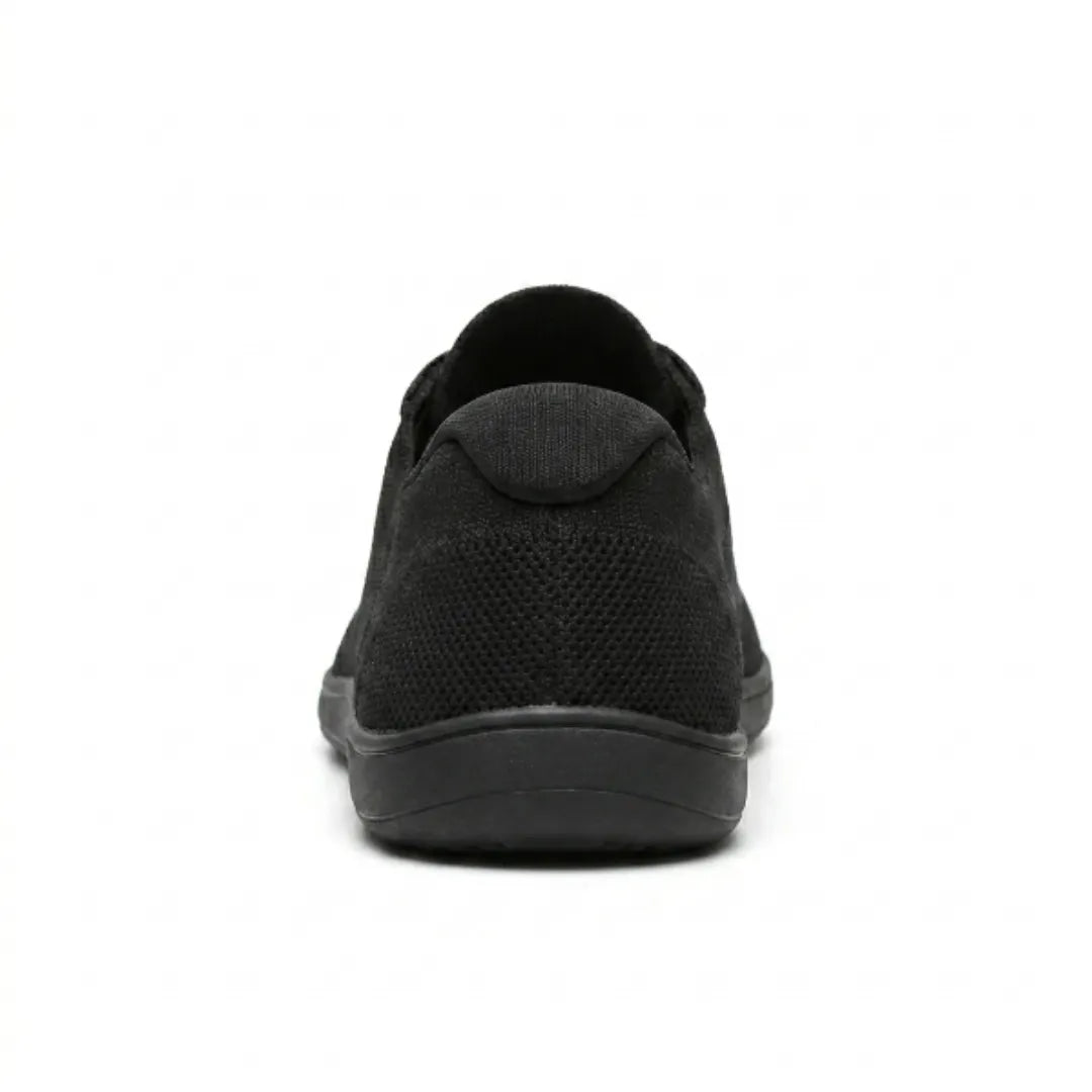 Schwarzer Sneaker von hinten, zeigt die gepolsterte Fersenkappe, das gelochte Mesh und die flache Sohle. 18