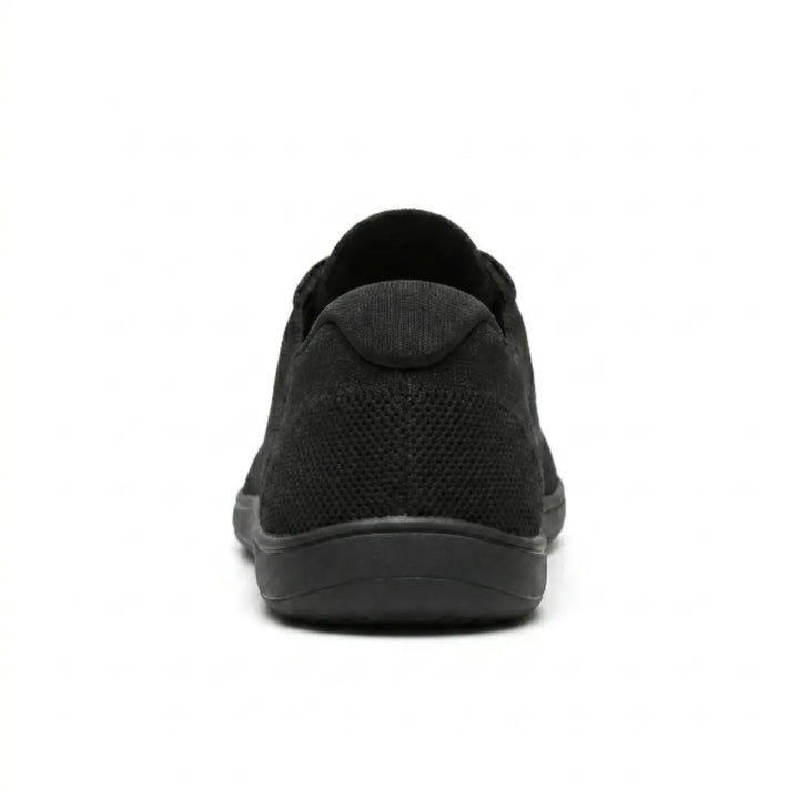 Schwarzer Sneaker von hinten, zeigt die gepolsterte Fersenkappe, das gelochte Mesh und die flache Sohle. 18