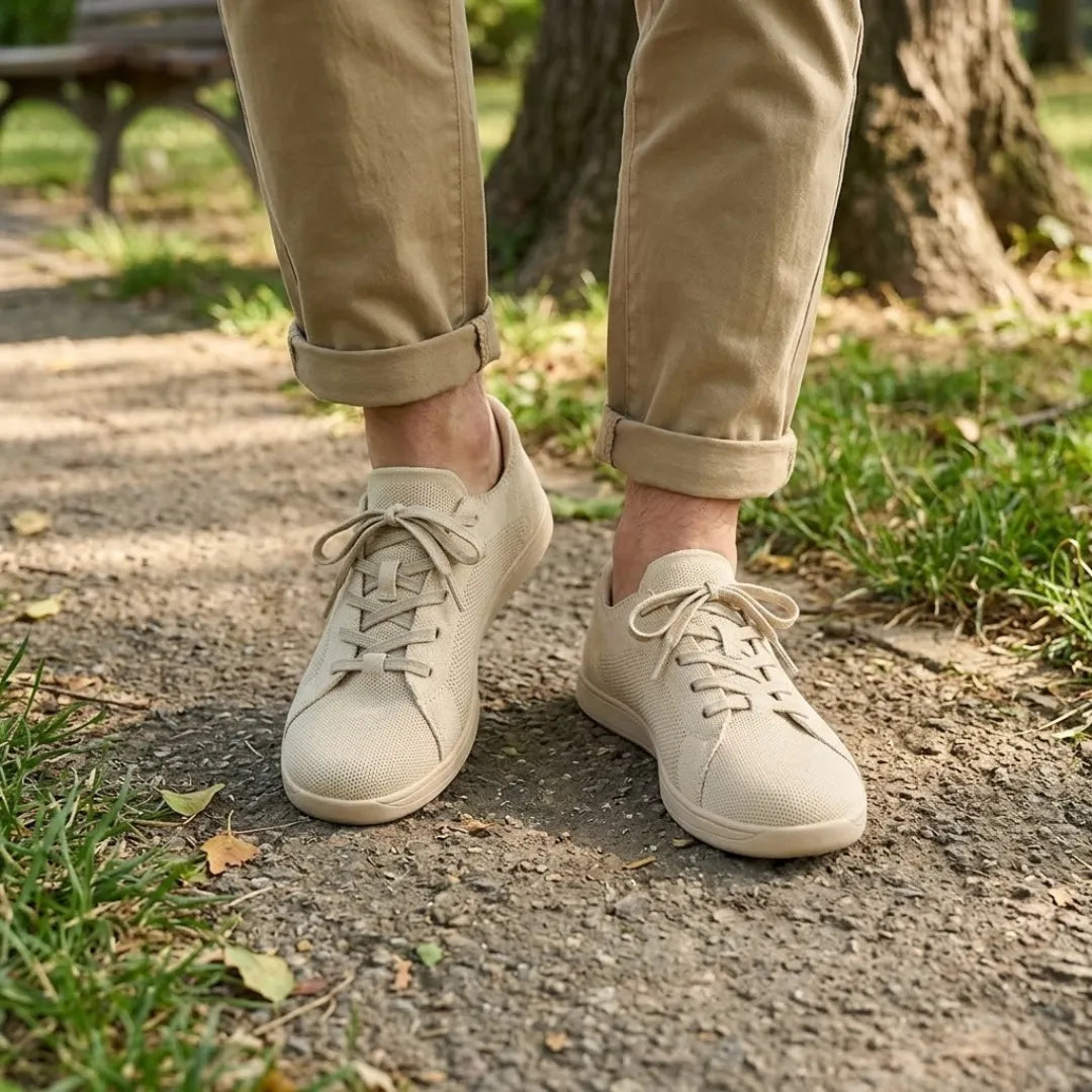 Beige Sneaker getragen auf einem Parkweg, dazu hochgekrempelte beige Hose, Gras und Baumstamm im Hintergrund. 2