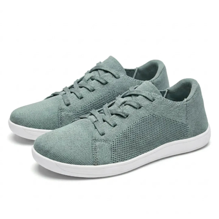 Paar graugrüne Barfuß-Sneaker aus Mesh mit weißer flacher Sohle und Schnürung, schräg von vorne auf weißem Hintergrund. 34