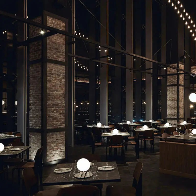Dunkles Restaurant mit Backsteinsäulen, auf dessen Tischen mehrere leuchtende Kugellampen als stimmungsvolle Beleuchtung stehen. 8