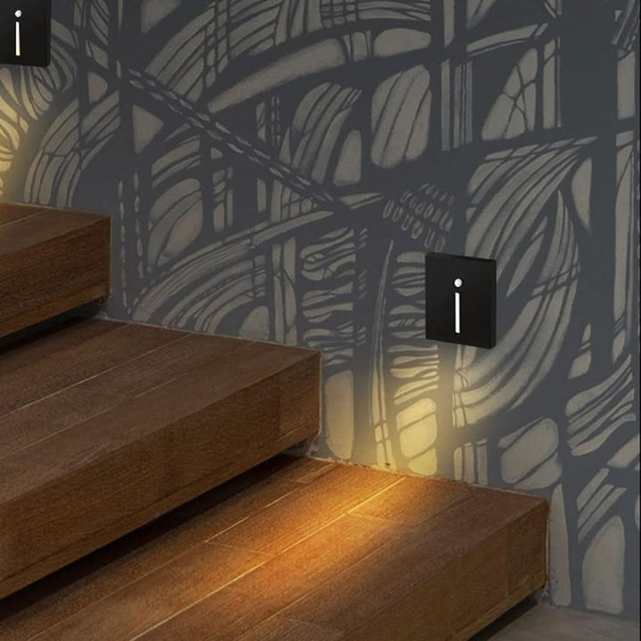 Zwei schwarze Wandleuchten mit schmalem Lichtschlitz beleuchten Holztreppenstufen vor einer grauen gemusterten Wand 2