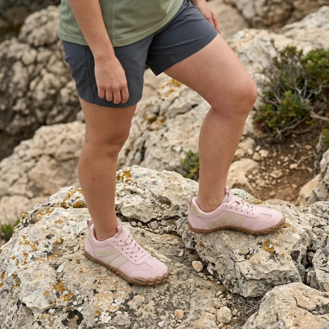 Frau in Shorts trägt rosafarbene Barfußschuhe und steht mit einem Fuß auf einem Felsen in felsiger Landschaft. 11