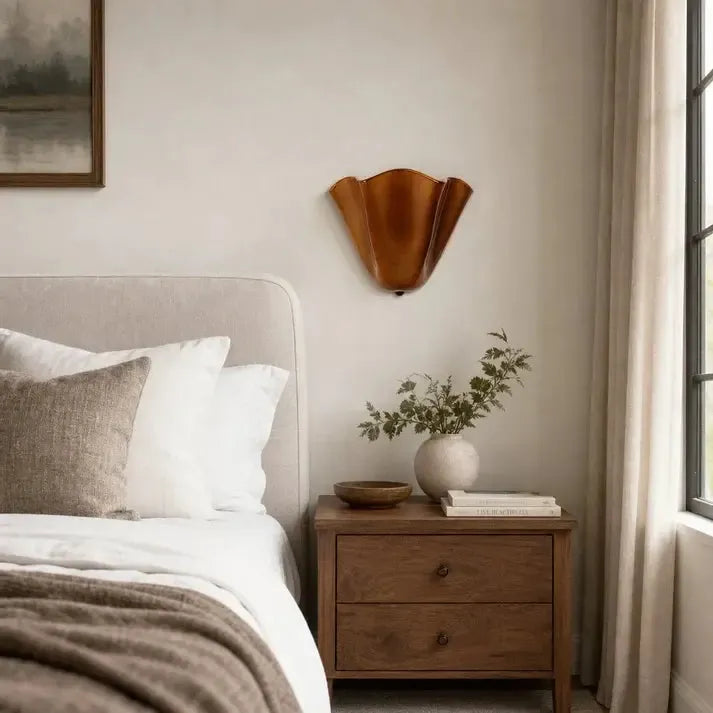 Ausgeschaltete bernsteinbraune Wandlampe mit welliger Form über einem Holznachttisch in einem hellen Schlafzimmer mit Vorhang. 3