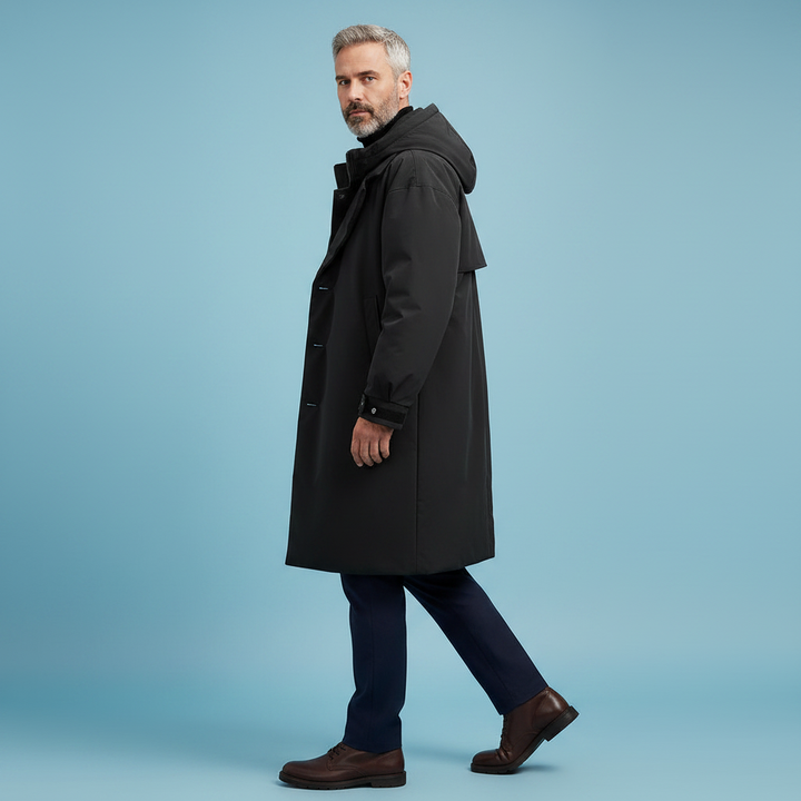Model im schwarzen Kapuzenmantel im Profil beim Gehen, mit dunkler Hose und braunen Schuhen vor hellblauem Hintergrund 6