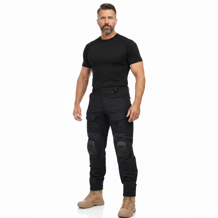 Bärtiger Model-Mann in schwarzem Shirt und schwarzer Hose mit Knieschonern, beigen Stiefeln, Ganzkörperansicht von vorn. 7