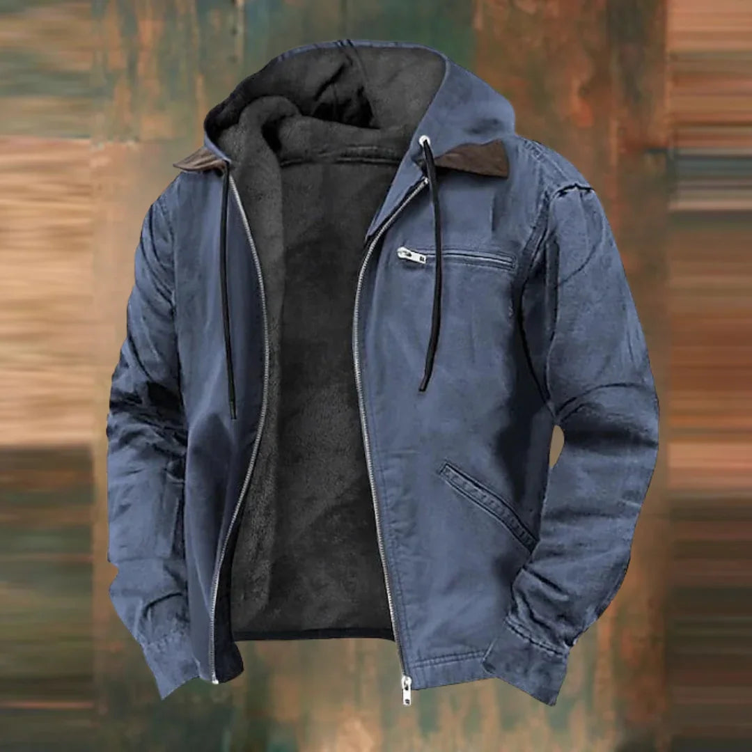 Dieselbe Jacke in Blaugrau, vorne offen mit Fleecefutter und Kapuze, vor einem verwaschenen braun-grünen Hintergrund. 2