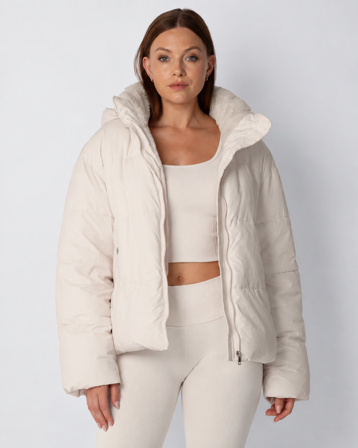 Frontansicht der cremefarbenen Steppjacke, offen getragen, mit flauschigem Kragen, ĂĽber passendem Crop-Top und Leggings 1