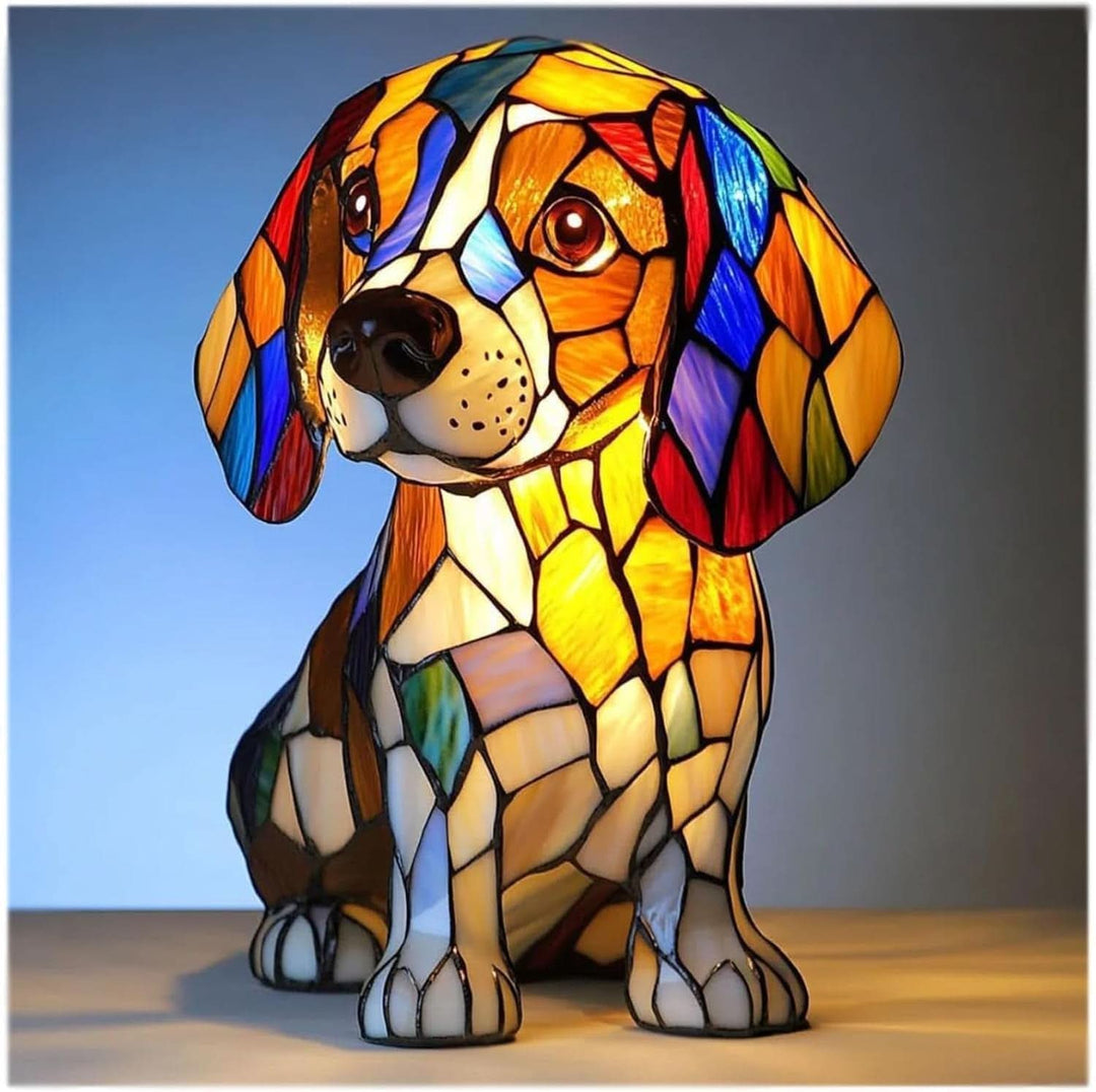Sitzender Welpe als leuchtende Buntglas-Figur mit Schlappohren in Orange, Blau und Rot, frontal vor blauem Hintergrund. 1