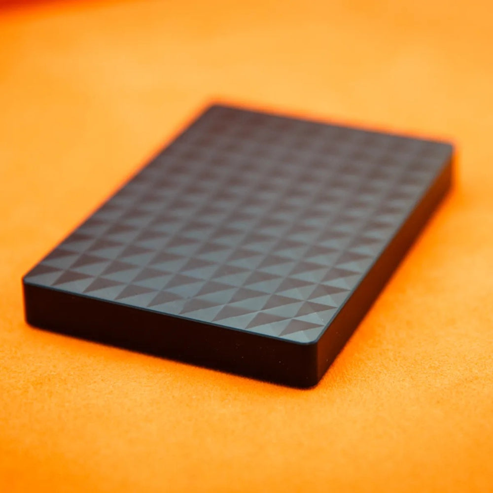 Flache schwarze Festplatte mit Rautenstruktur schräg von oben auf orangefarbenem Untergrund 4