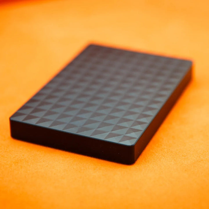Flache schwarze Festplatte mit Rautenstruktur schräg von oben auf orangefarbenem Untergrund 4