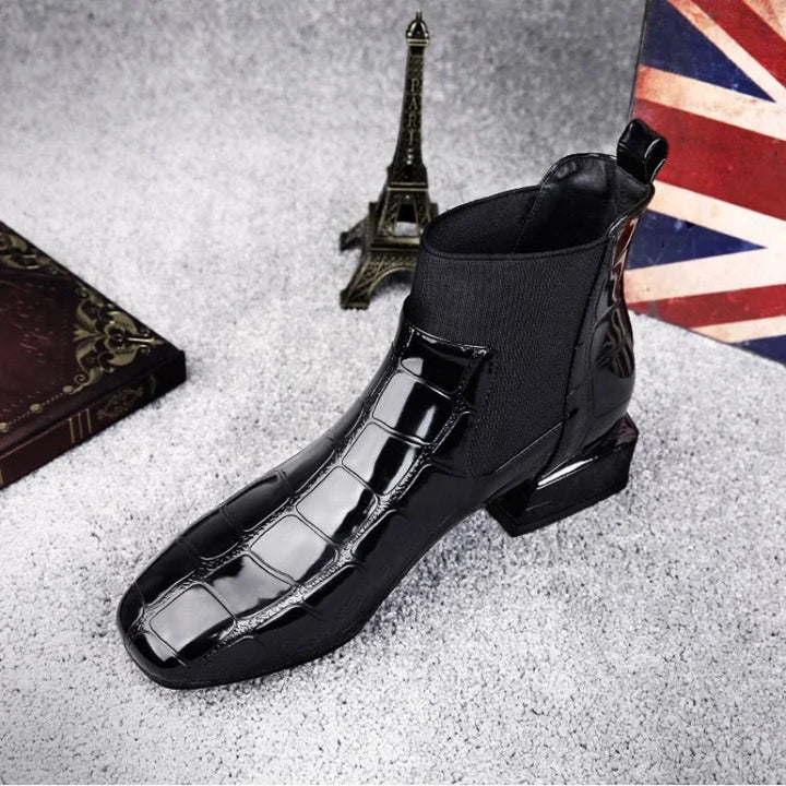 Schwarzer glänzender Stiefel mit Krokoprägung und elastischem Einsatz, schräg von oben auf grauem Teppich neben Eiffelturm-Figur fotografiert. 1