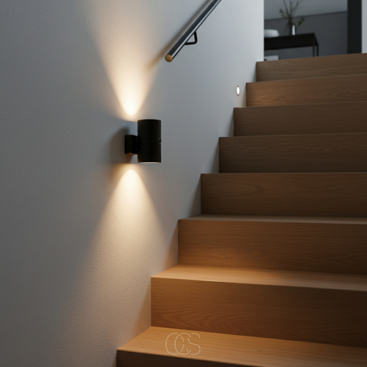 Schwarze Nachtlampe an der Wand neben einer Holztreppe mit Handlauf wirft einen warmen Lichtkegel nach oben und unten. 5