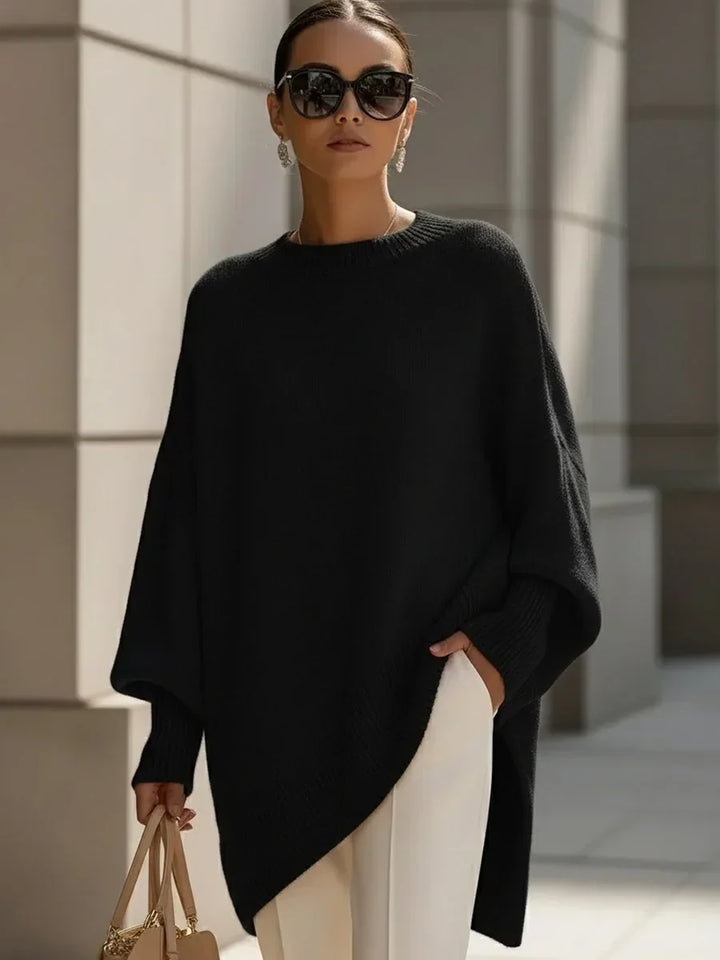 Schwarzer Pullover mit weiten Ärmeln und asymmetrischem Saum, getragen mit weißer Hose, heller Handtasche und Sonnenbrille. 6
