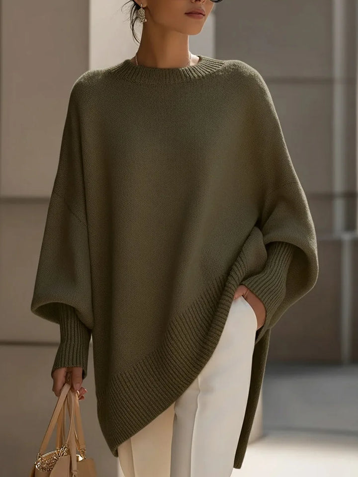 Olivgrüner Pullover mit Fledermausärmeln und schrägem Rippsaum, kombiniert mit weißer Hose und heller Handtasche. 7