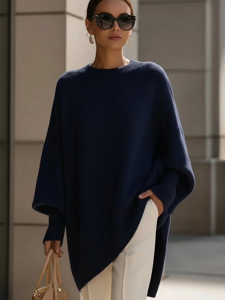 Dunkelblauer Pullover mit weitem Schnitt und asymmetrischem Saum, getragen von einer Frau mit Sonnenbrille und weißer Hose. 8