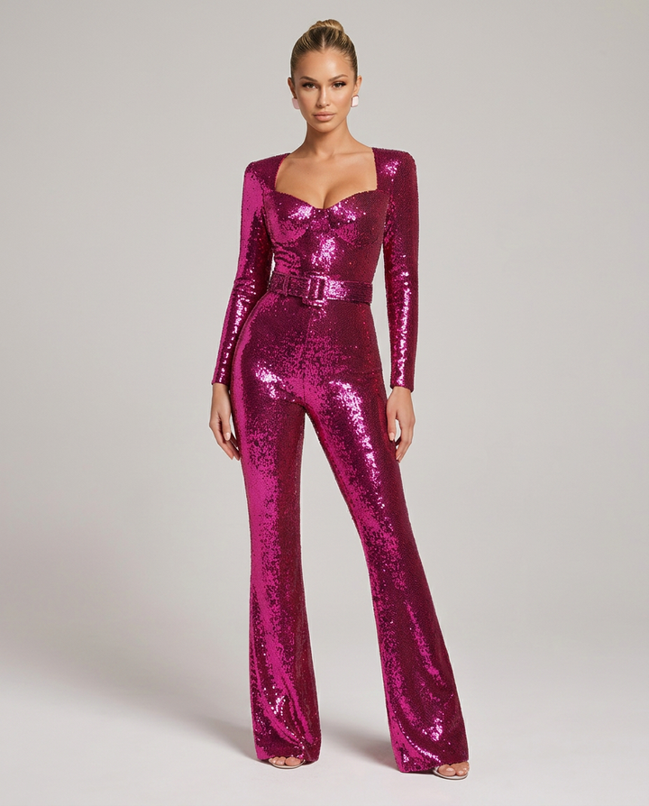 Frontansicht des pinken Pailletten-Overalls mit Herzausschnitt, langen Ärmeln, Gürtel in der Taille und ausgestellten Hosenbeinen, getragen von einem Model. 1