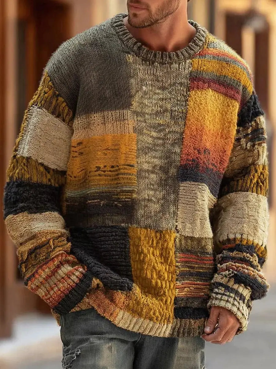 Mann trägt einen Rundhals-Strickpullover mit gelben, grauen und orangen Patchwork-Flächen, Frontansicht mit Jeans auf der 1